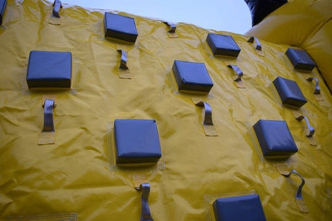 Close-up of yellow inflatable obstacle course climbing wall with gray padded steps and sturdy hand grips for traction